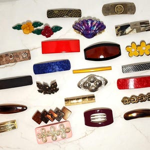 Könnte beinhalten: Eine Sammlung von fünfundzwanzig verschiedenen Haarspangen und Clips in diversen Formen, Farben und Mustern, darunter florale, muschelförmige, geometrische und einfarbige Designs aus Kunststoff, Metall und Harz, die verstreut angeordnet sind.