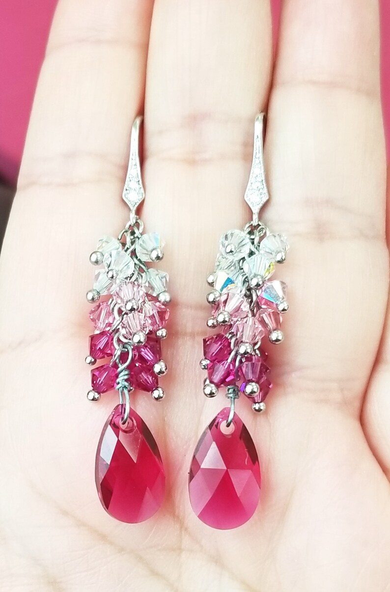 Peut inclure: Une paire de boucles d'oreilles pendantes en argent avec une cascade de perles de cristal roses, rouges et claires. Les boucles d'oreilles pr&eacute;sentent un cristal en forme de larme au bas.