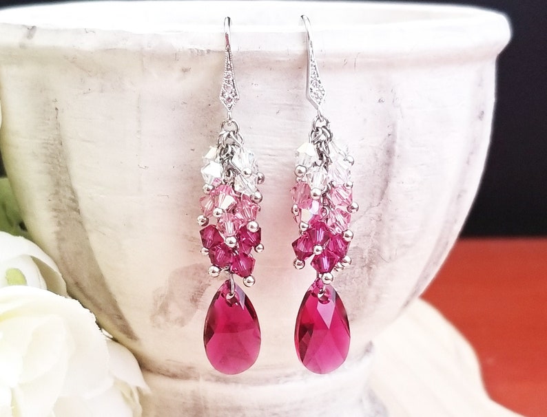 Peut inclure: Une paire de boucles d'oreilles pendantes argent&eacute;es avec un d&eacute;grad&eacute; de cristaux roses, blancs et transparents. Les boucles d'oreilles pr&eacute;sentent un cristal en forme de larme au bas.