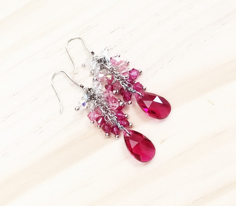 Peut inclure: Une paire de boucles d'oreilles pendantes argent&eacute;es avec un d&eacute;grad&eacute; de cristaux roses et transparents. Les boucles d'oreilles pr&eacute;sentent un cristal en forme de goutte d'eau au bas.