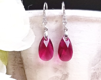 May include: A pair of silver dangle earrings with teardrop-shaped red crystal stones.