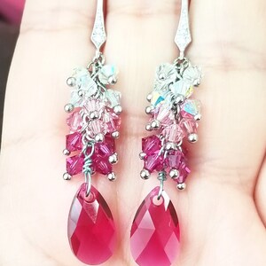 Peut inclure: Boucles d'oreilles pendantes argent&eacute;es avec un cristal rouge en forme de larme et une cascade de petits cristaux dans des tons de rose, blanc et iris&eacute;.