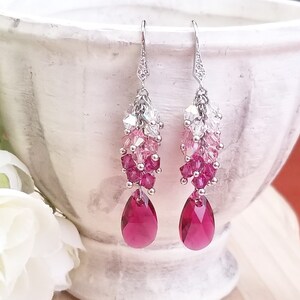Peut inclure: Une paire de boucles d'oreilles pendantes argent&eacute;es avec un d&eacute;grad&eacute; de cristaux roses et clairs, se terminant par un cristal rouge rubis en forme de larme.