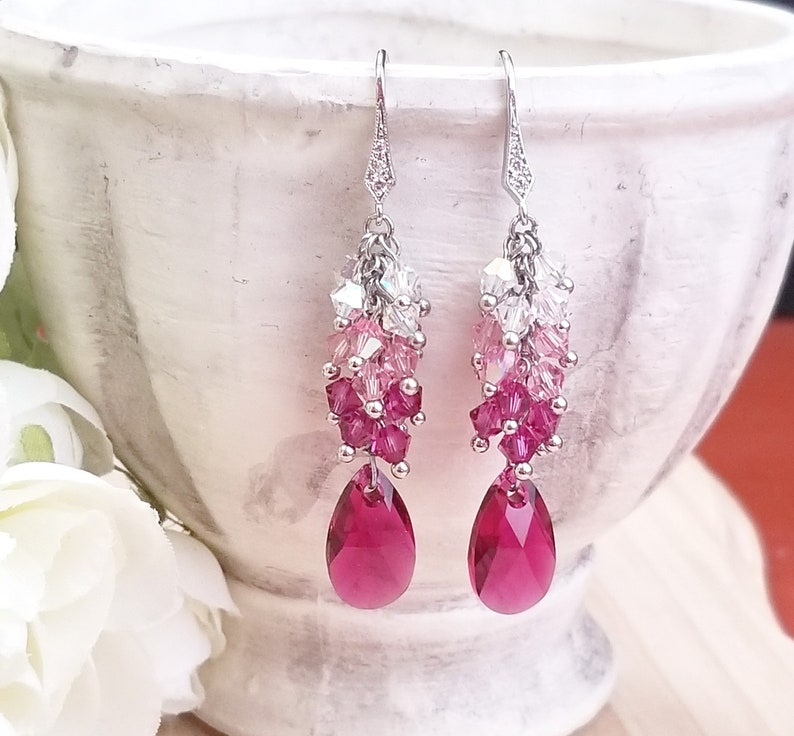 Peut inclure: Une paire de boucles d'oreilles pendantes argent&eacute;es avec un d&eacute;grad&eacute; de cristaux roses et clairs, se terminant par un cristal rouge rubis en forme de larme.