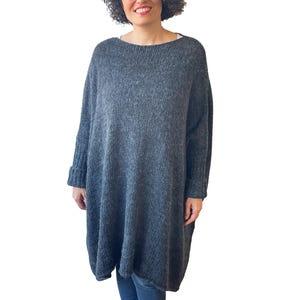 May include: A gray, oversized sweater dress with a boat neck and long sleeves. The dress has a relaxed fit and ribbed cuffs. The fabric appears to be a soft knit, perfect for cooler weather. The dress is knee-length.