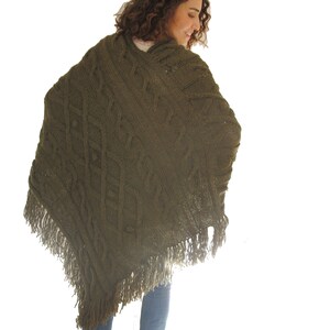 May include: A green knitted poncho with a cable knit pattern and fringe trim.