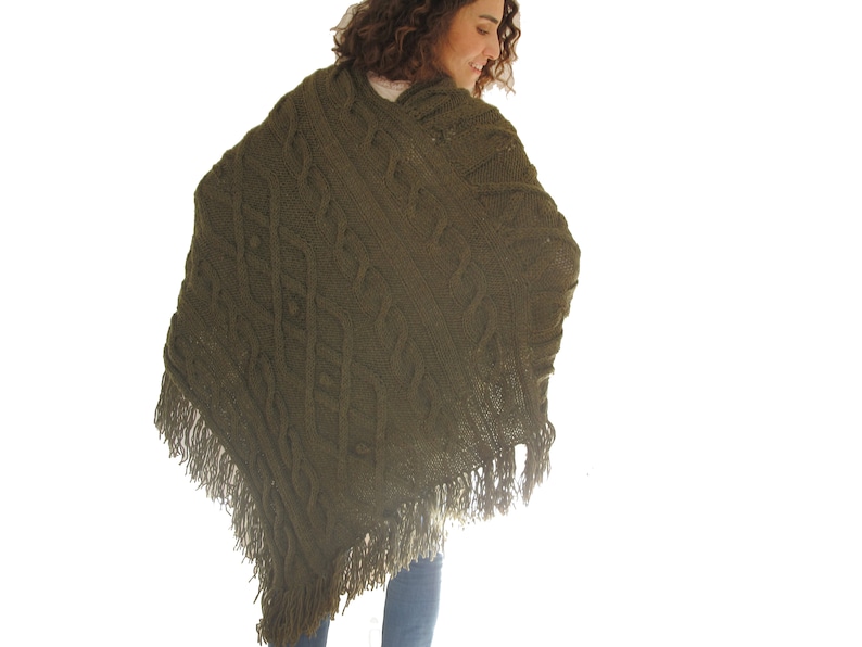 May include: A green knitted poncho with a cable knit pattern and fringe trim.