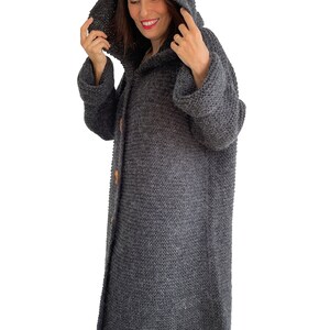May include: A long, gray knitted cardigan with a hood and button closure. The cardigan is made of a soft, fuzzy yarn.