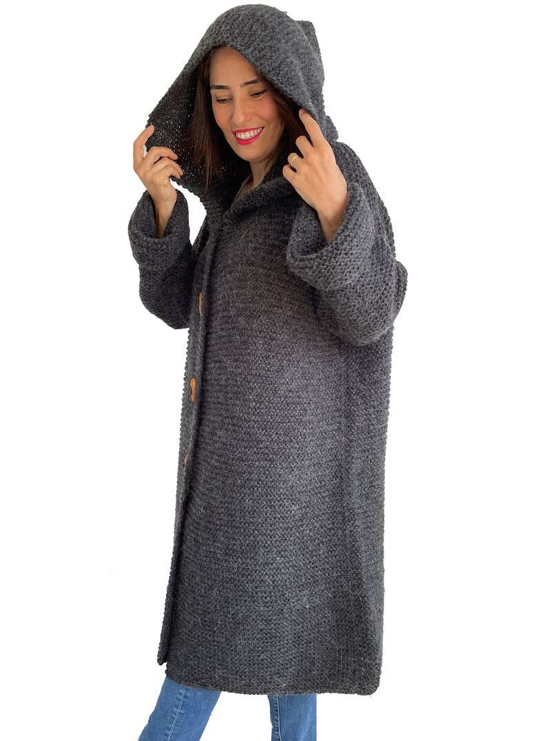 May include: A long, gray knitted cardigan with a hood and button closure. The cardigan is made of a soft, fuzzy yarn.