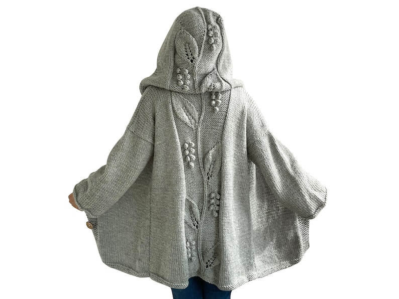 K&ouml;nnte beinhalten: Ein grauer Strickcardigan mit Kapuze und einem Blumendesign auf der R&uuml;ckseite. Der Cardigan hat eine lockere Passform und lange &Auml;rmel.