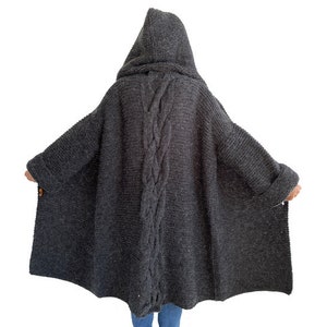 May include: A long, dark gray knitted cardigan with a hood and a braided detail down the back.