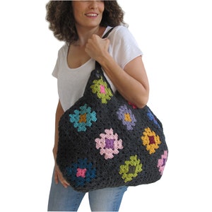 May include: A large, black crochet tote bag with colorful granny squares. The bag has a leather strap and is being held by a person.