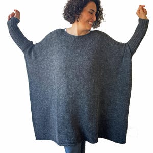 May include: A dark gray, oversized knit sweater with long sleeves. The sweater has a wide, loose fit and a round neckline. The sleeves are ribbed at the cuffs. The model is wearing the sweater.