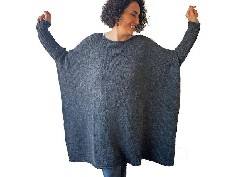 May include: A dark gray, oversized knit sweater with long sleeves. The sweater has a wide, loose fit and a round neckline. The sleeves are ribbed at the cuffs. The model is wearing the sweater.