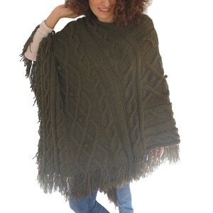 May include: A green knitted poncho with fringe detailing. The poncho has a cable knit pattern.