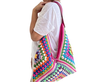 Könnte beinhalten: Eine bunte gehäkelte Tragetasche mit einem rosafarbenen Riemen. Die Tasche ist aus verschiedenen Farben gefertigt, darunter Rot, Orange, Gelb, Grün, Blau, Lila und Pink.
