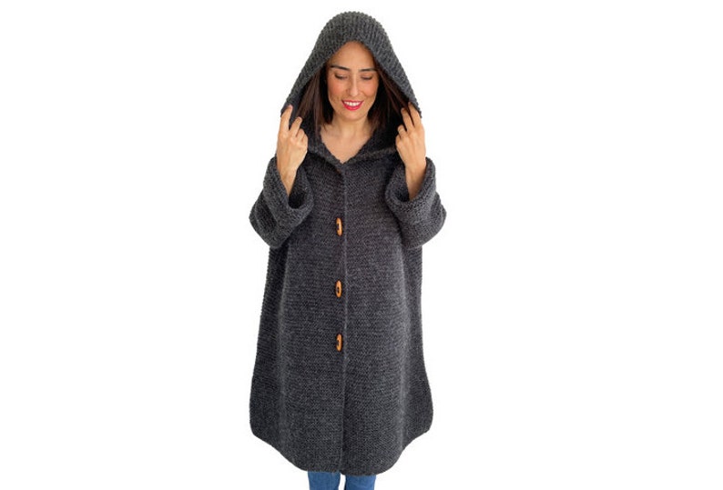 May include: A long, dark gray hooded cardigan with wooden buttons. The cardigan is knitted and has a relaxed fit.