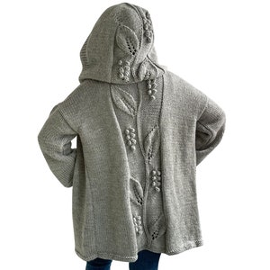 K&ouml;nnte beinhalten: Ein grauer Kapuzenpullover mit einem in den R&uuml;cken gestrickten Blatt- und Beerenmuster.