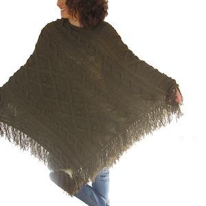 May include: A green knitted poncho with a cable knit pattern and fringe trim.