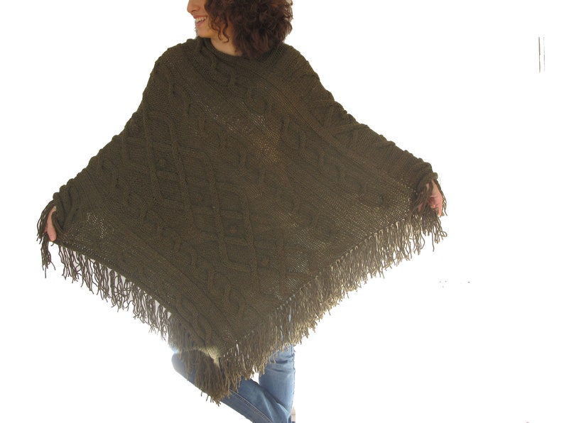 May include: A green knitted poncho with a cable knit pattern and fringe trim.