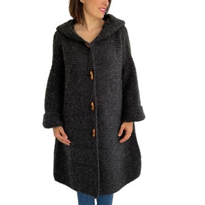May include: A long, gray knitted cardigan with a hood and wooden buttons. The cardigan has a relaxed fit and a slightly flared hem.