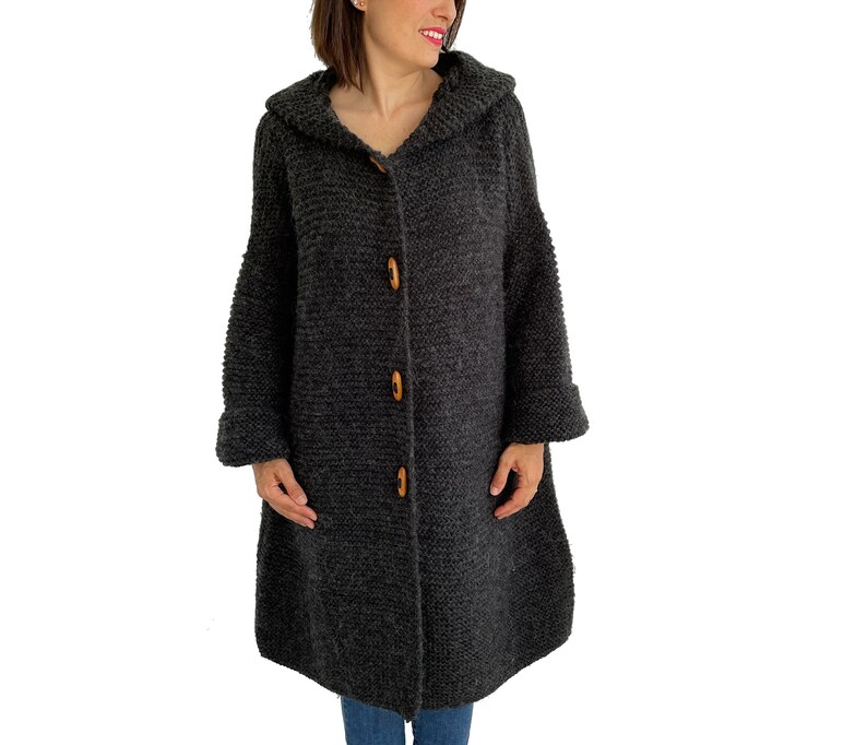 May include: A long, gray knitted cardigan with a hood and wooden buttons. The cardigan has a relaxed fit and a slightly flared hem.