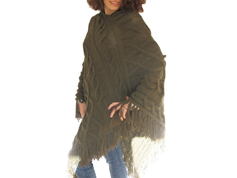 May include: A green knitted poncho with a cable knit pattern and fringe trim.