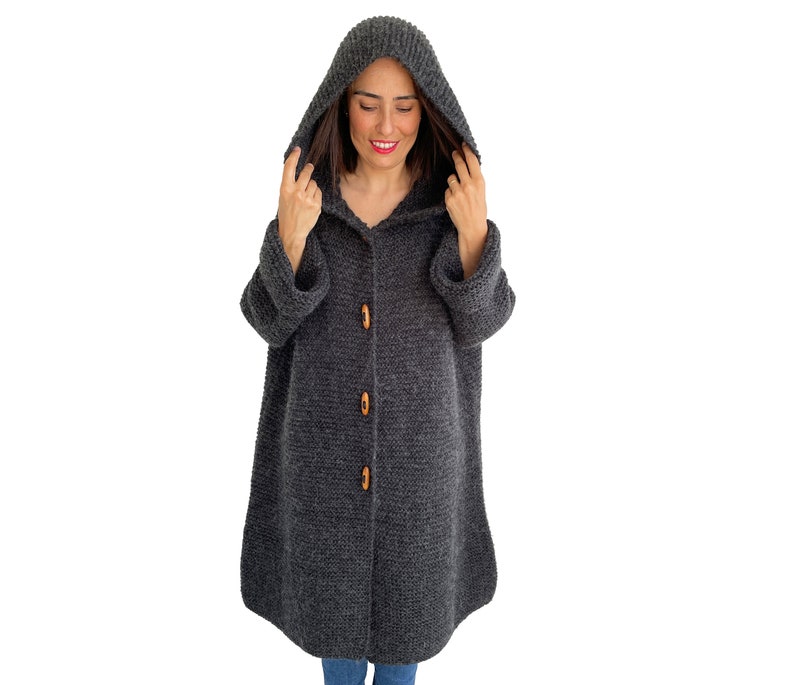 May include: A gray hooded cardigan with wooden buttons. The cardigan is knitted and has a long, loose fit.