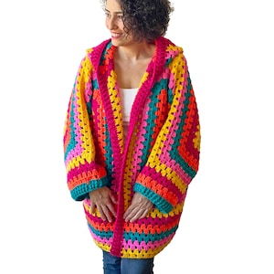 May include: A vibrant, handmade crochet hooded cardigan in a patchwork design. The colorful garment features a mix of pink, yellow, teal, and orange squares. The open-front sweater has long sleeves and a hood, perfect for adding a pop of color to any outfit.