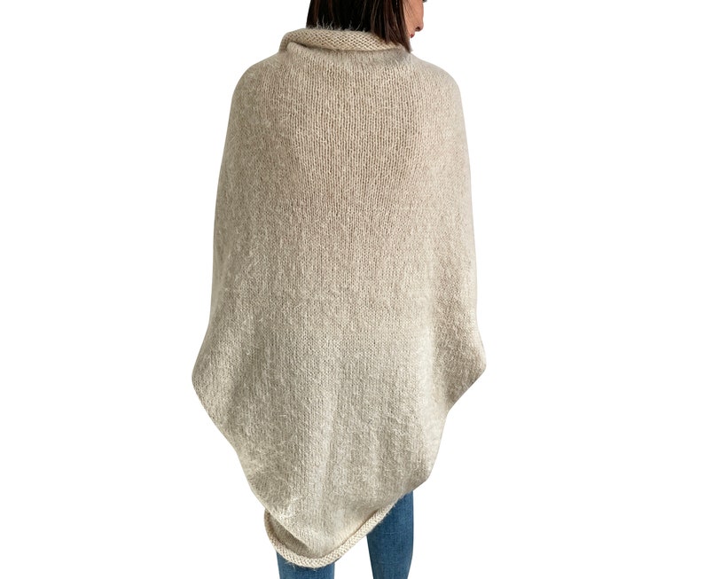 Puede incluir: Un poncho de punto beige con cuello alto y un corte suelto y fluido.