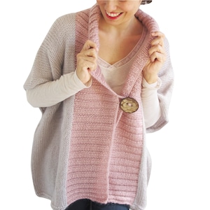May include: A pink and gray knitted cardigan with a large wooden button. The cardigan has a wide collar and a loose fit.