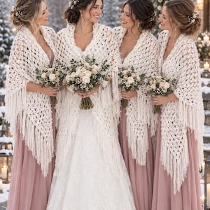 Puede incluir: Cuatro personas visten vestidos largos de color rosa polvoriento hasta el suelo y chales de ganchillo color crema con flecos largos. Cada persona sostiene un ramo de rosas blancas y follaje. Los chales presentan un patrón de tejido abierto.