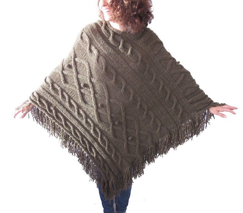 May include: A green knitted poncho with a cable knit pattern and fringe trim.