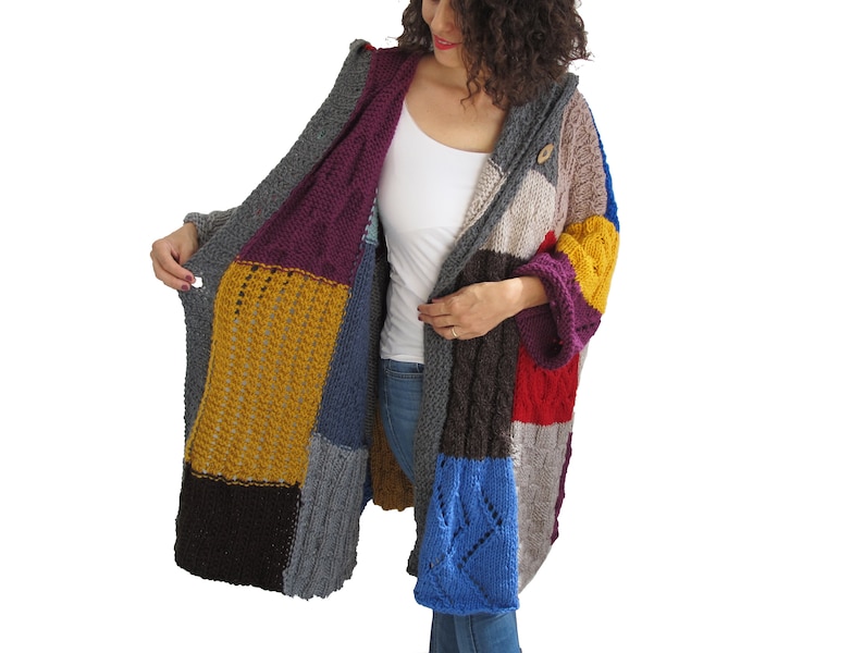 May include: A long, multi-colored knitted cardigan with a hood. The cardigan is made of different colored squares of knit fabric, including purple, yellow, blue, red, and brown. The cardigan has a button closure at the neck.
