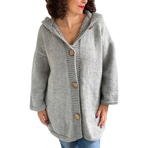 K&ouml;nnte beinhalten: Ein grauer Kapuzenpullover mit Holzkn&ouml;pfen. Der Pullover ist gestrickt und hat eine lockere Passform.