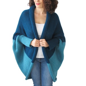 May include: A blue and teal knitted cardigan with a shawl collar and long sleeves. The cardigan is open in the front and has a relaxed fit.