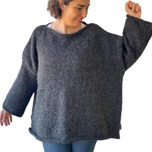 Peut inclure: Un pull ample gris foncé avec des manches longues. Le pull a une encolure bateau large et une coupe ample et confortable. Le tricot semble être fait d'un fil doux et texturé, parfait pour les temps plus frais.
