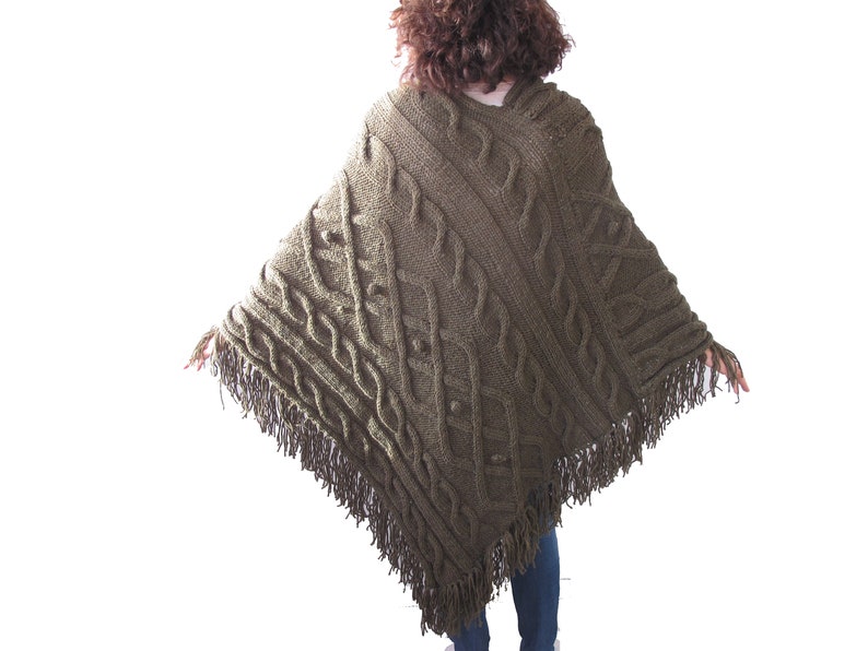 May include: A green knitted poncho with a cable knit pattern and fringe trim.