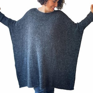 May include: A dark gray, oversized knit sweater with long sleeves. The sweater has a wide, boat neck and a loose, comfortable fit. The sleeves have ribbed cuffs. The sweater is made of a soft, textured yarn.