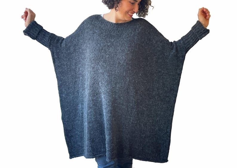 May include: A dark gray, oversized knit sweater with long sleeves. The sweater has a wide, boat neck and a loose, comfortable fit. The sleeves have ribbed cuffs. The sweater is made of a soft, textured yarn.