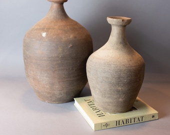 May include: Two terracotta vases, one larger than the other, with a book titled "HABITAT" in front of them.