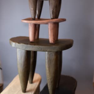 May include: Four wooden stools stacked on top of each other. The stools are all different colors and have a unique, three-legged design.