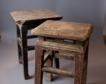 May include: Two antique wooden stools with a dark brown finish. The stool on the right has a red paint accent. Both stools have a simple, square design.