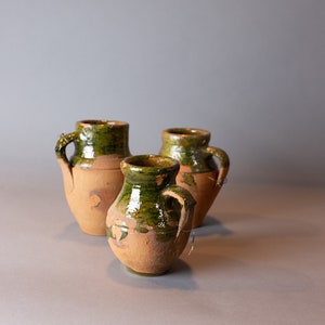 May include: Three terracotta pottery jugs with green glaze. The jugs have a rounded body and a small handle on the side.