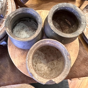 May include: Three rustic brown ceramic bowls with a rough, textured surface. The bowls are sitting on a wooden surface.
