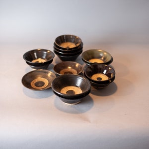 May include: A collection of small, black ceramic bowls with a white and brown design. The bowls are stacked and arranged on a white surface.