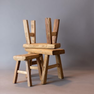 May include: Three wooden stools stacked on top of each other. The stools are made of natural wood and have a rustic look.