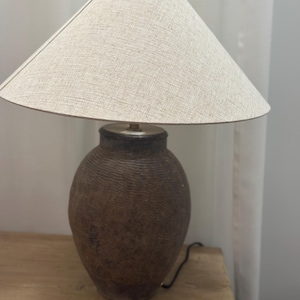 May include: A brown ceramic table lamp with a beige linen lampshade. The lamp has a textured, ribbed surface.