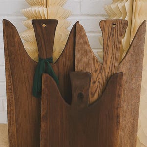 May include: A collection of wooden cutting boards in various shades of brown. Each board has a unique shape with a handle, and one is adorned with a green ribbon. The boards are displayed against a white brick wall and decorative paper cutouts.