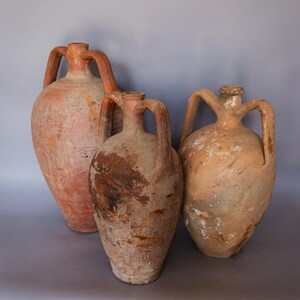 May include: Three terracotta amphorae with handles, two are brown and one is a lighter brown with white streaks.